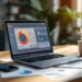 Laptop displaying colorful analytics dashboards and graphs on wooden desk with smartphone, printed reports, and coffee cup