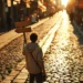 Entrepreneur at crossroads holding wooden signpost, choosing between multiple cobblestone paths lined with storefronts in golden sunlight.