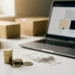 Stapel euromunten en bonnetjes naast laptop met productpagina, kleine verzenddozen op wit bureau in zacht natuurlijk licht.