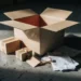 Open Amazon shipping box on warehouse floor with smaller boxes, crumpled invoices, and price tag tangled in brown packing tape spilling out.