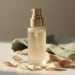 Premium skincare bottle on white surface with scattered petals and linen cloth, warm golden-hour light casting soft shadows.