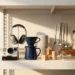 Flat lay of bestselling electronics, kitchen gadgets, toys, and home goods on a white warehouse shelf with warm golden side lighting.