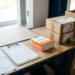 Printed e-commerce seller dashboard checklist on a warehouse packing desk beside a shopping bag and stacked cardboard boxes ready for dispatch.