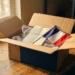 Open cardboard shipping box with a French tricolor flag, bubble wrap, and folded invoice on a warehouse desk in warm amber light.